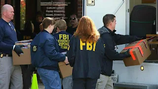 A photo of FBI agents carrying boxes and bags out of a house in Paris, Illinois, with a police car parked outside.