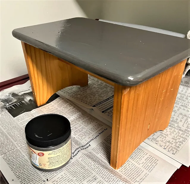 Photo of the top of a wooden stool being painted in dark gray.