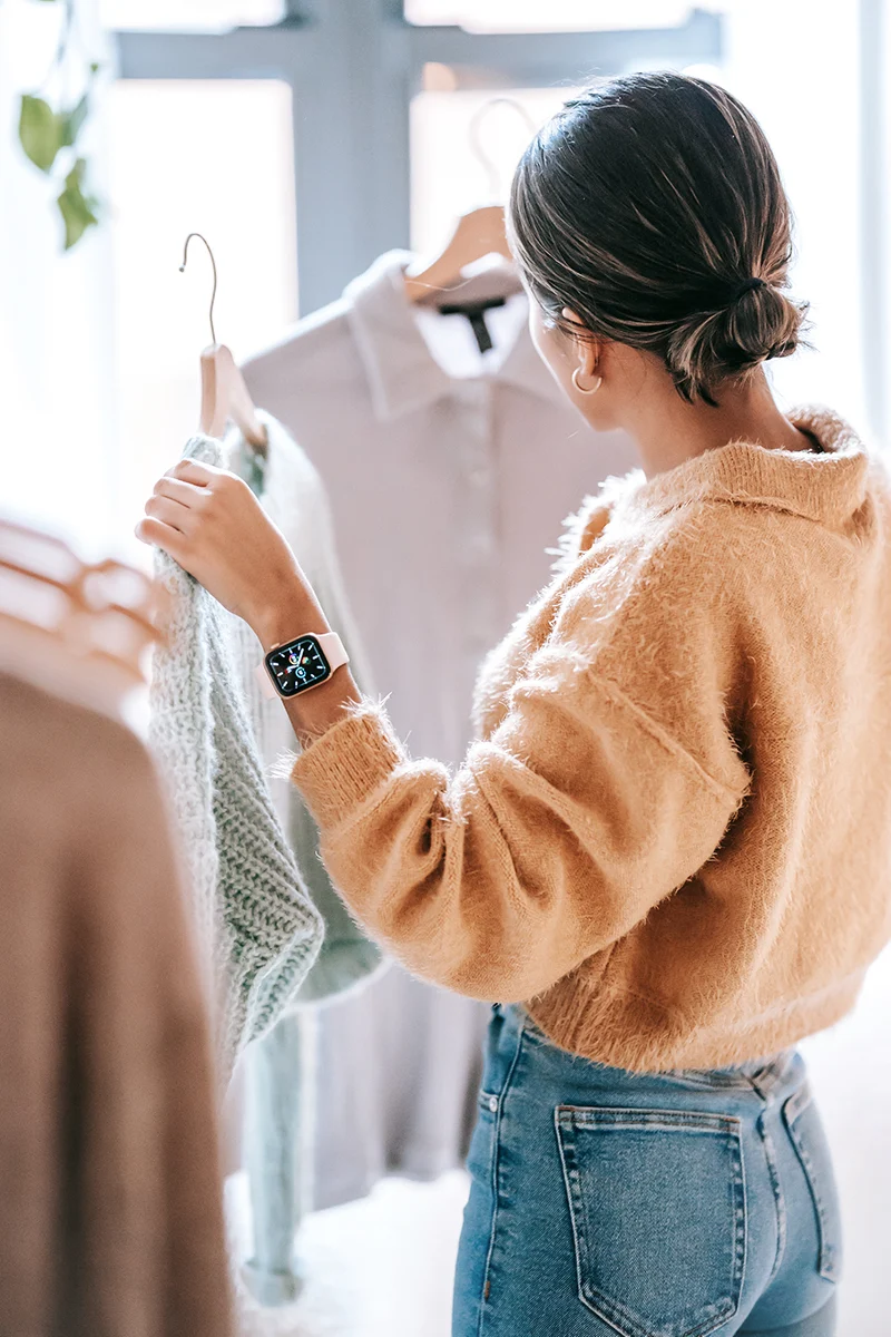 woman in stylish outfit reassessing her wardrobe and golds two sweaters in her hands