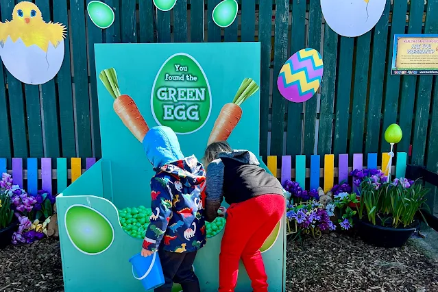 Children grabbing a green egg and putting in a bucket as part of the Marsh Farm Easter Egg Hunt 2023