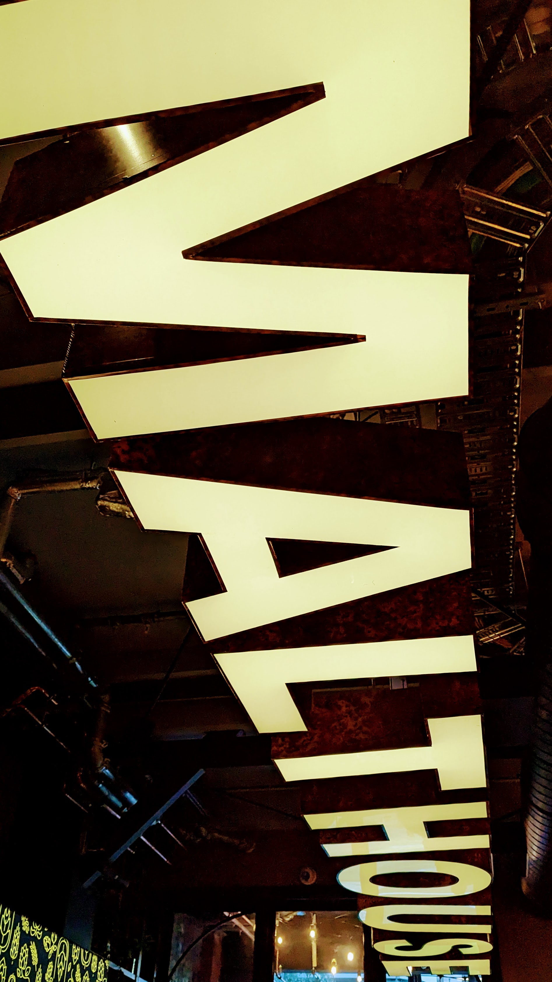 Very large, yellow, cut out letters of 'Malthouse' on the dark ceiling