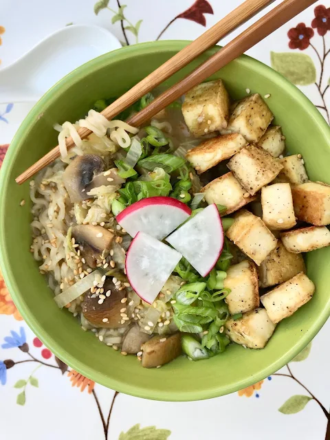 Finished bowl of tofy and mushroom miso ramen bowls with chopsticks pulling out some noodles.