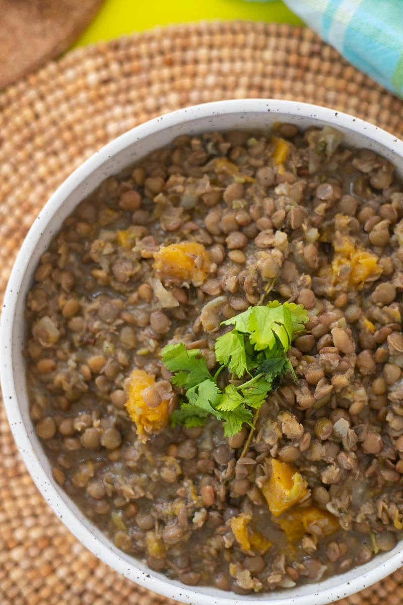 A large bowl of stewed lentils on garnished with scallions, on top of a brown place mat.