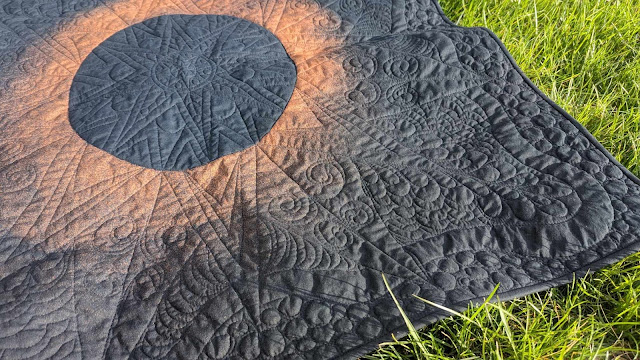 Solar eclipse quilt made with bleached black fabric and free motion quilting