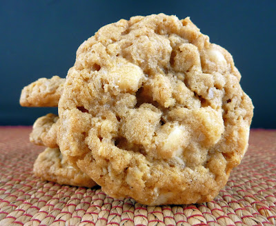 A cinnamon white chocolate oat cookie resting against a stack of the same cookies, photographed on a natural woven mat with red thread