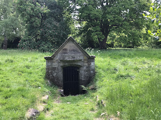 A photo showing a small stone building with a metal, gated door.  This is the building that covers the Oyly Well in Liberton, Edinburgh.  Photograph by Kevin Nosferatu for the Skulferatu Project.