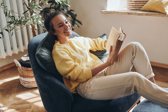 A person sitting in a comfortable chair, holding a book and looking relaxed