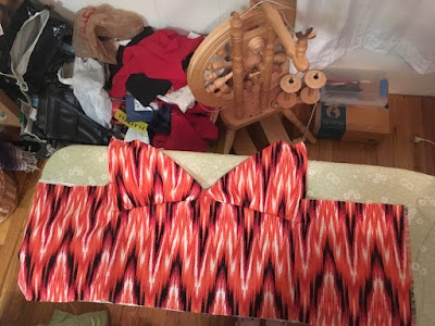 A coral, black, and white fake-ikat sundress bodice, laid out on a green ironing board.