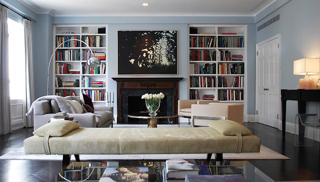 jarlath mellett's living room fireplace suround by a wood mantel, built in bookshelves filled with books, a grey sofa, neutral cushioned bench and dark wood floors.