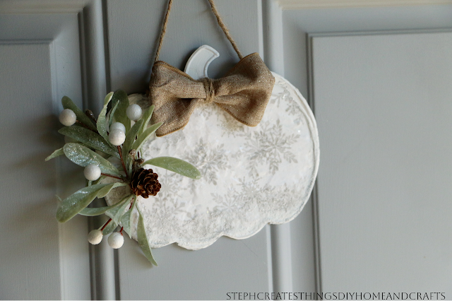 Metal pumpkin with snowflake pattern, holiday foliage, and bow being displayed on a door