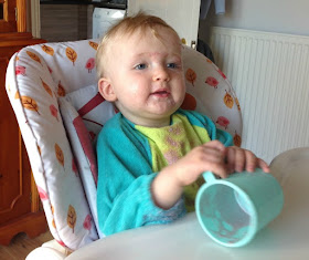 Toddler in highchair with empty cup and contents on his face and bib