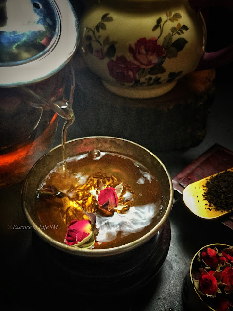 "A teapot surrounded by dried rose petals and loose tea leaves, symbolizing the process of crafting Chinese Rose Tea."