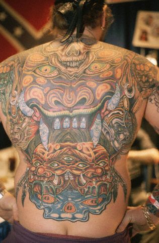 Dragon head, skulls, and monster tattoo all over man's back.