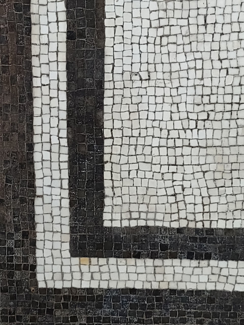 Rectangular detail of a mosaic. a band of black tiles around the left and bottom of the frame; a band of white tiles within that; a band of black tiles within the white band. The remaining tiles in the upper right form a rectangle and they're all white. Each tile is a very small, irregular square.