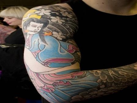 Tattoo of a Japanese girl surrounded with flowers on arm