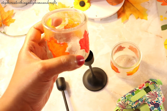 Hand holding up a glass jar that has been decorated with faux leaves