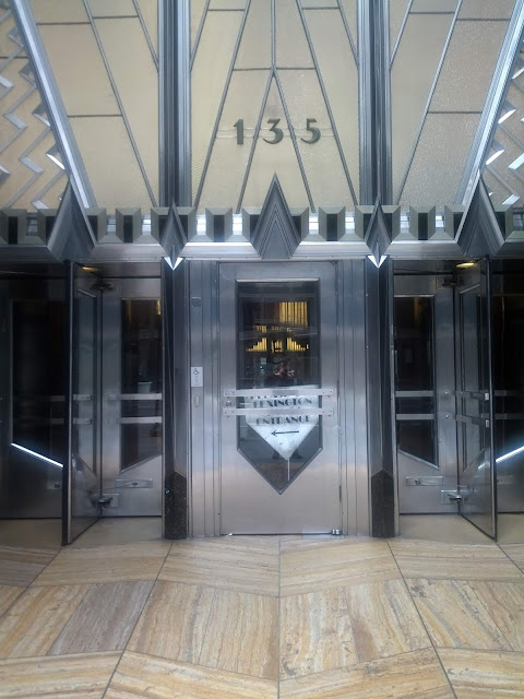 Art Deco style stainless steel doors with chevron-shaped glass windows and stone flooring in a fancy pattern.