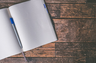 an image of a blank open notebook, with a pen, on a wooden table