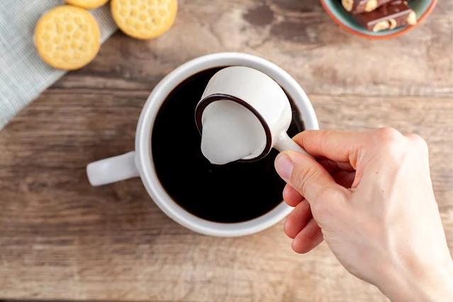 Adding a creamer to a cup of black coffee.