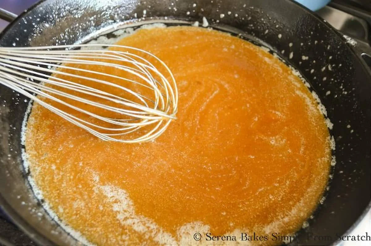 Sugar being whisked into melted butter in a cast iron pan.