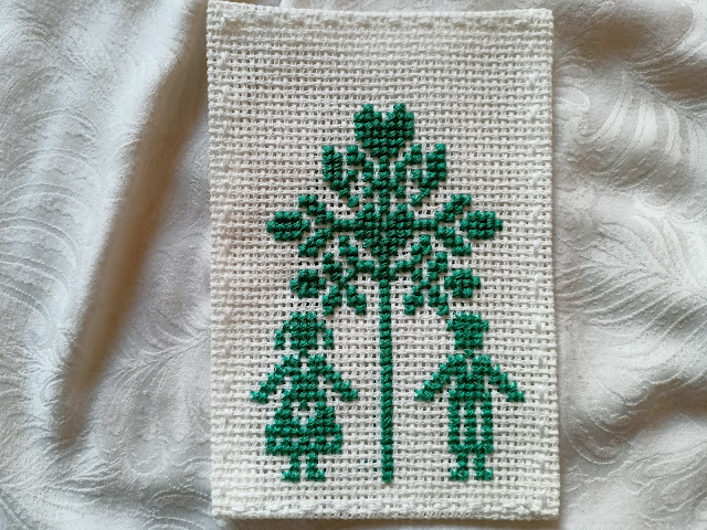 Zielona wyszywanka drzewko miłości, pod kórym po lewej jest dziweczynka, a po prawej chłopiec