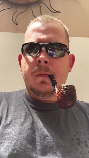 Handsome pipe smoker wearing sunglasses in a gray t-shirt puffing from the neck up