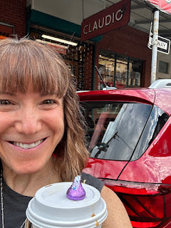 A selfie of me holding a coffee with a Hershey's Kiss on top in front of my new red car.