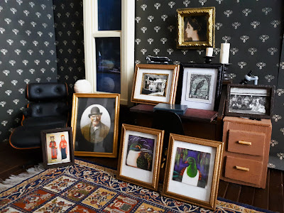 Selection of one-twelfth scale framed pictures propped up against furniture in a dark academia study scene.