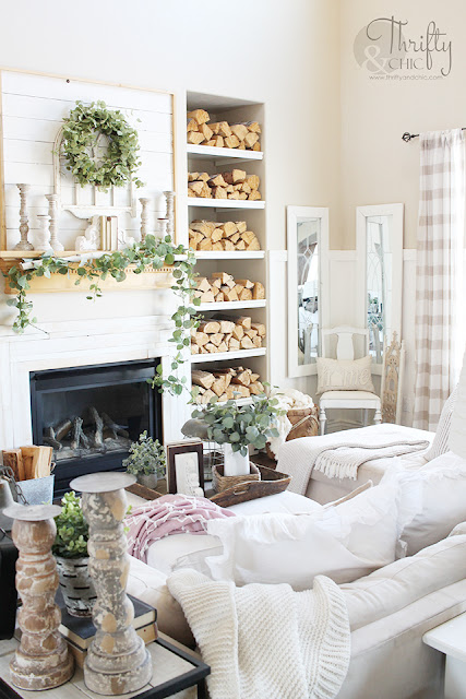 living room with white couch, large window, stacked wood, and shiplap mantel