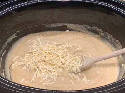 Cooked cauliflower soup in a slow cooker with grated smoked cheese on top