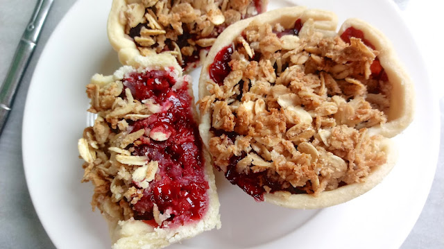 a Blackberry Granola Mini Breakfast Pie sitting on a plate next to another pie that has been cut in half to expose the filling