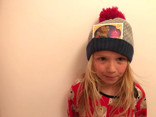 A reluctant child posing with a woolly hat on and a beast card in the folded up flap at the bottom