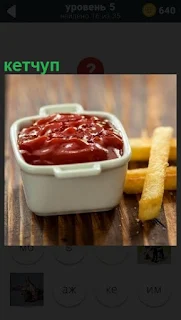 На столе в лоточке находится кетчуп и рядом картошка фри