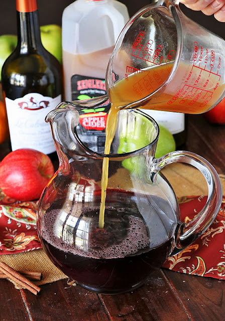 Pouring Autumn Apple Sangria Ingredients into a Pitcher Image