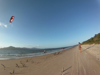 Kitesurf en la playa de Daniela y manglares naciendo en la arena. Mujer mirando todo parada en la playa con vestido al viento.