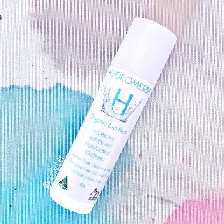 Retail packaging for Hydromerse Lip Balm,  a white tube with a white label on a white/pink/blue watercolour background.