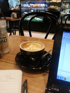 A photograph of a cup of coffee, laptop and notepad in a cafe.