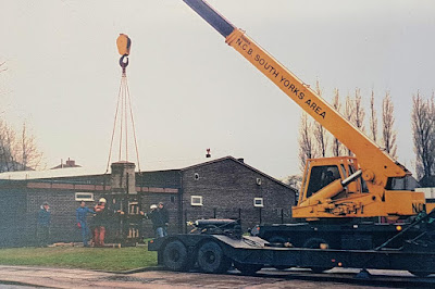 Men guiding a war memorial into position as it is held aloft by a large crane
