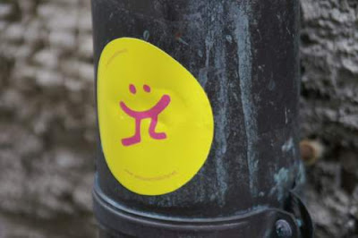 Graffiti sticker image of a 'Happy Face' which is eating somebody... only the lower legs are sticking out of the mouth, from the old town centre of Genoa, Italy.