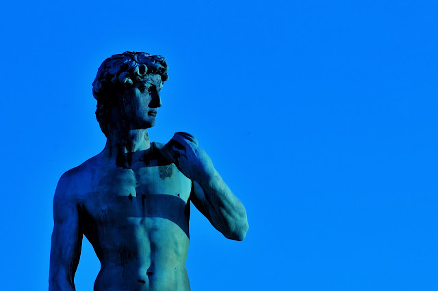 Riproduzione dalla cintola in su del David di Michelangelo sotto una luce e davanti a uno sfondo entrambi blu