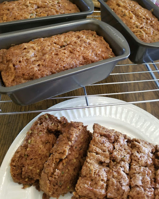 Zucchini bread sliced on a plate and loaves cooling on a rack