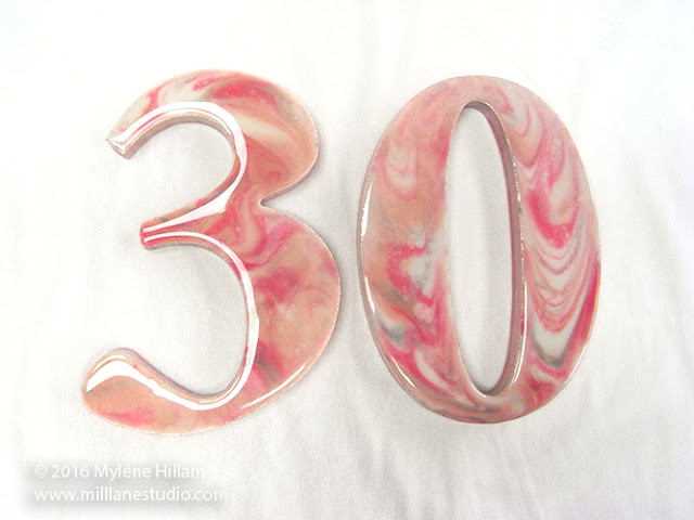 Glossy, marbled resin in shades of pink, silver and white on wooden numbers, 3 and zero.