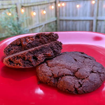 One cookie cut in half to show the melty center, with a backdrop of a back yard fence with lights illuminated along it.