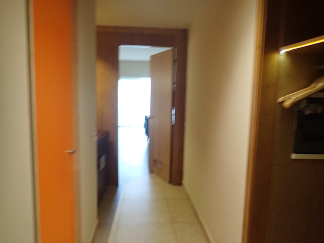 Hotel suite hallway with orange door on the right, and open closet on the left. A door at the end leads to the bedroom/living area.