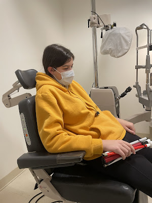 You sitting in the ophthalmology office waiting in the chair for the dr to come in. You are wearing a mask, black leggings, and your yellow sweatshirt. Your can is across your lap folded up.