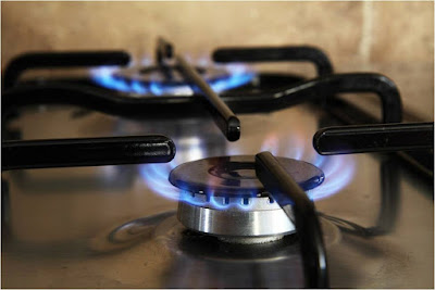 A gas stove top turned on with flames coming out below the grate