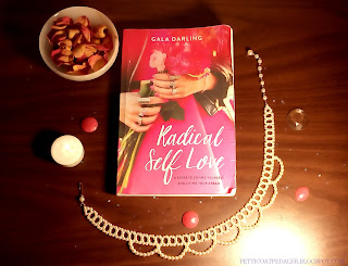 Flat lay of Gala Darlings book Radical Self Love with a tea candle, bowl of dried rose petals, a pearl necklace, and pink and clear gems.  
