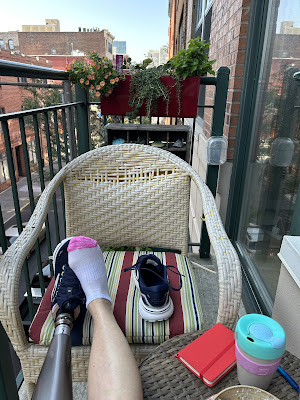 A view of my feet resting on a balcony chair - the left prosthetic, the right in a sock with a sneaker sitting next to it.