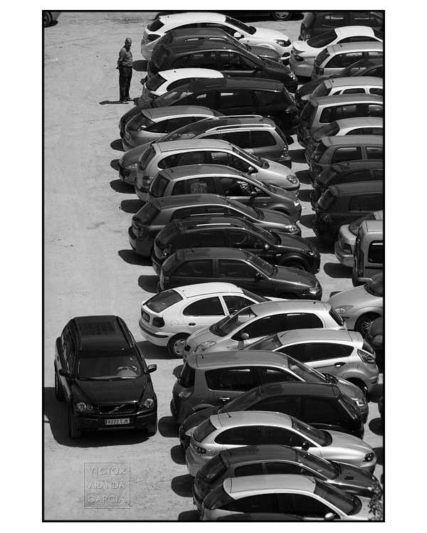 Fotografía en blanco y negro de muchos coches aparcados en un solar.