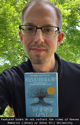 Adam against a backdrop of trees holding a copy of The Buried Giant